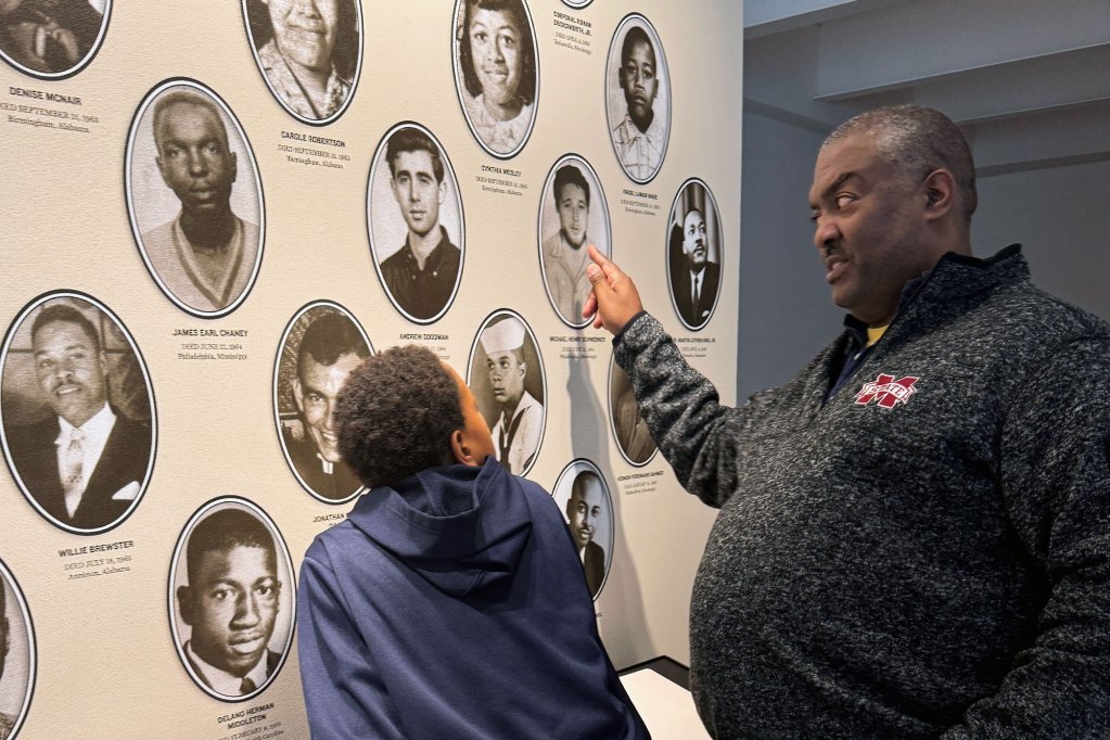 a father points out photos on a museum exhibit wall to his son