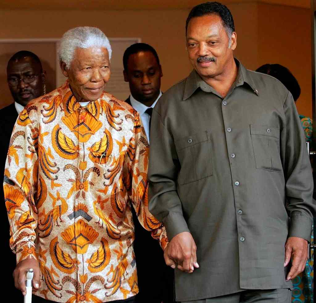 Jesse Jackson holds Nelson Mandela's hand as Mandela walks with a cane in the other hand