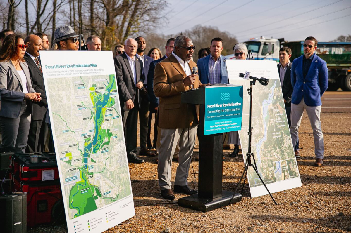 photo of a man speaking with people behind him and maps on either side