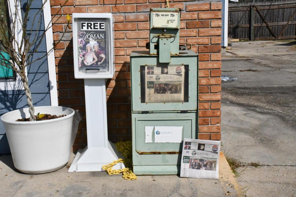 Two newspaper stands sit outside of a storefront. One says FREE and one has a 75¢ coin lock