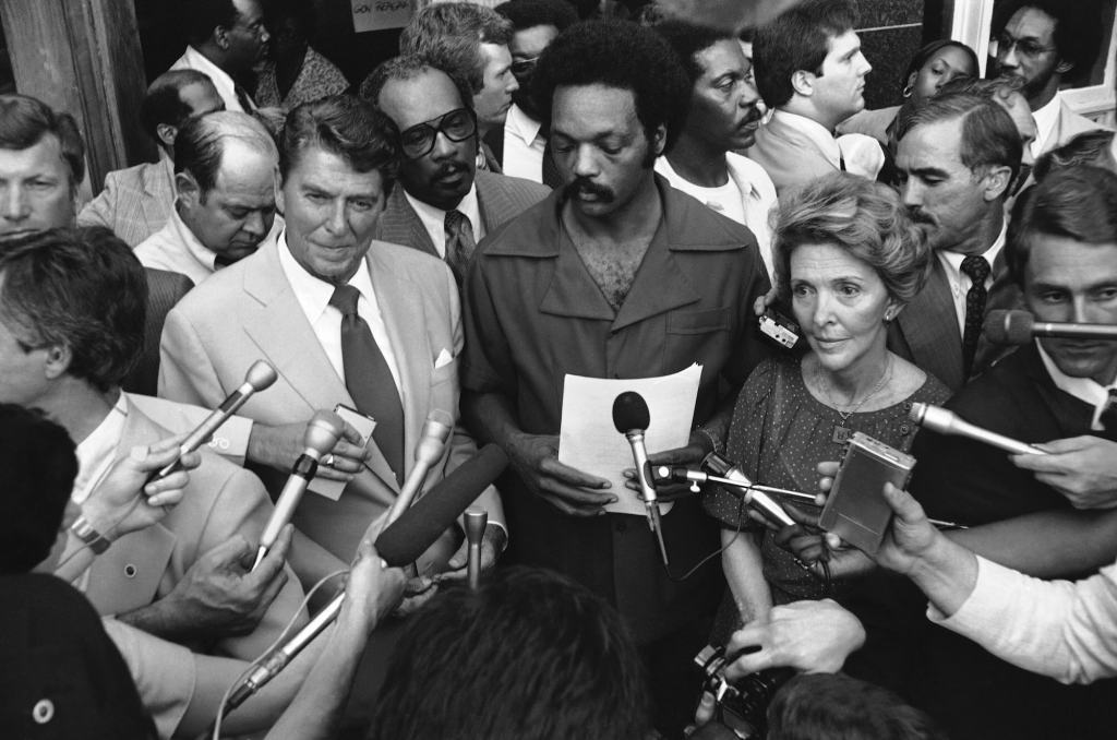 A black and white image of Jesse Jackson speaking to reporters alongside Ronald Reagan