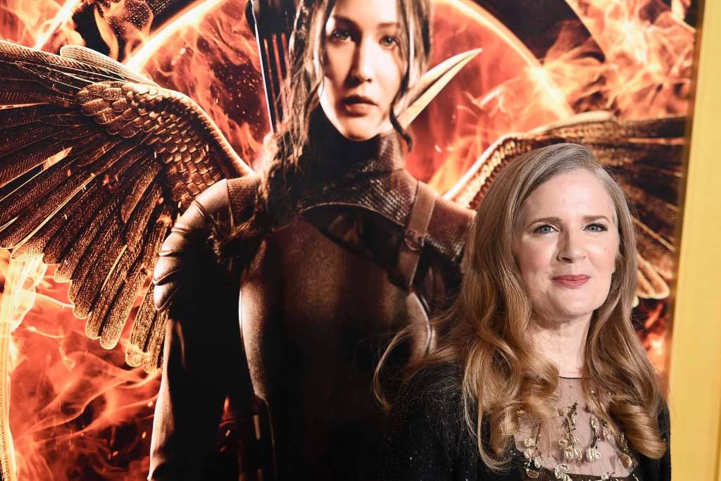 A woman stands next to a poster of a movie character wearing an armored suit with wings.