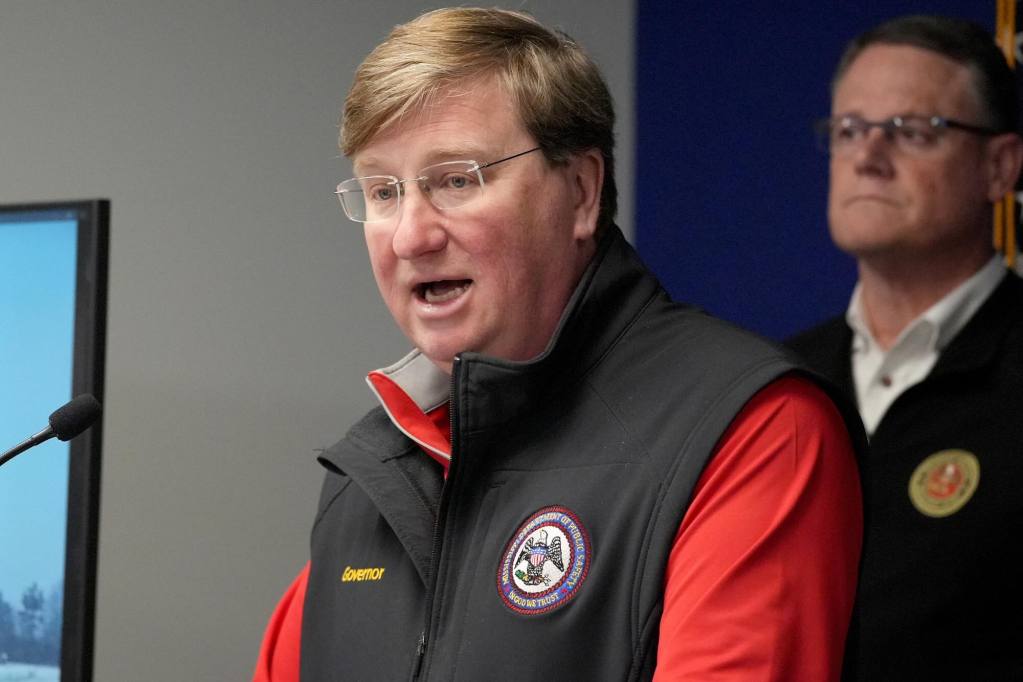 Tate Reeves speaking at a lectern wearing a black vest over a red shirt