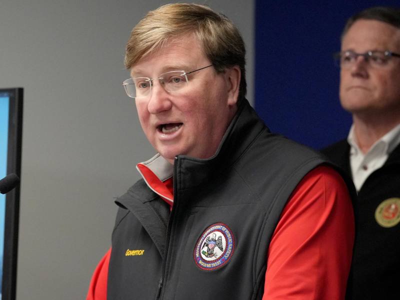 Tate Reeves speaking at a lectern wearing a black vest over a red shirt