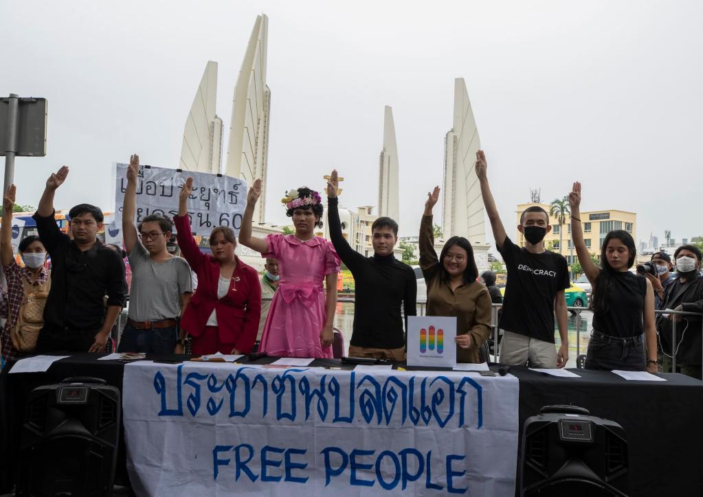 Several people hold up a banner while saluting with three fingers outstretched. Thai script is written on the banner along with “Free people” written in English.