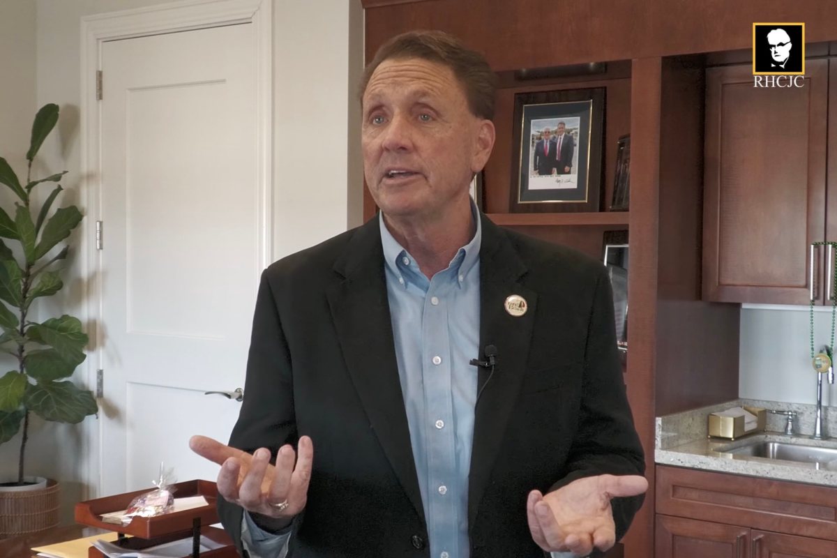 A man wearing a black suit jacket and blue button-up shirt speaking.