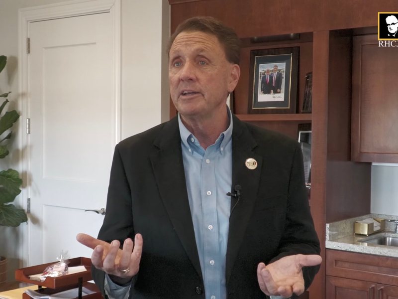 A man wearing a black suit jacket and blue button-up shirt speaking.