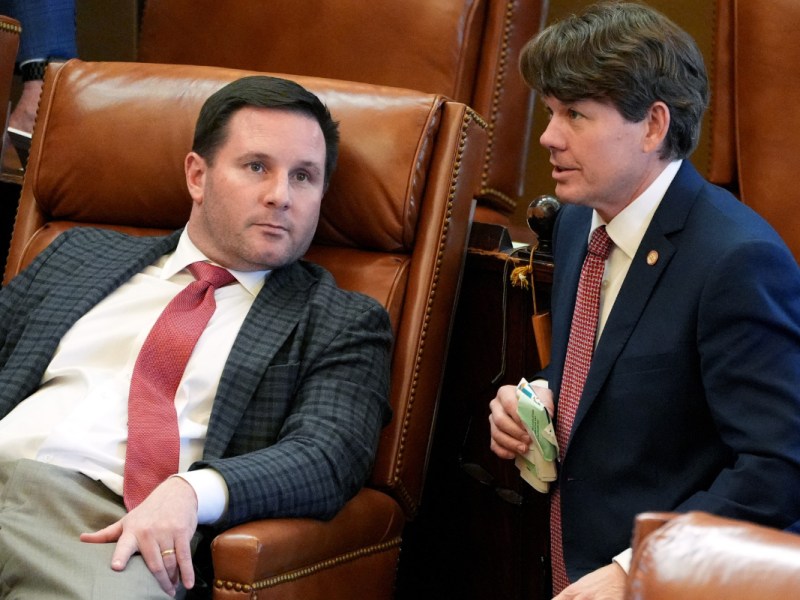 Rep. Trey Lamar leans back in a brown leather chair while Rep. Joey Hood crouches next to him on the right.