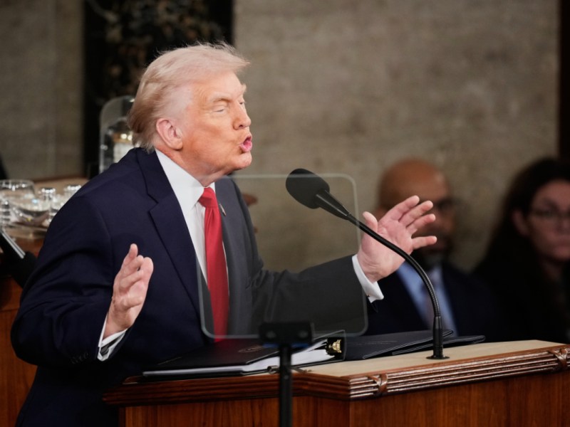 Donald Trump speaking at a podium with lights from the upper gallery shining down.
