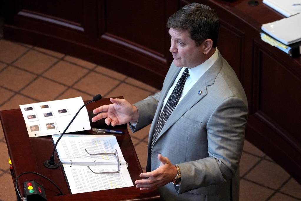 William Quin II, in a light grey suit, speaking at a podium