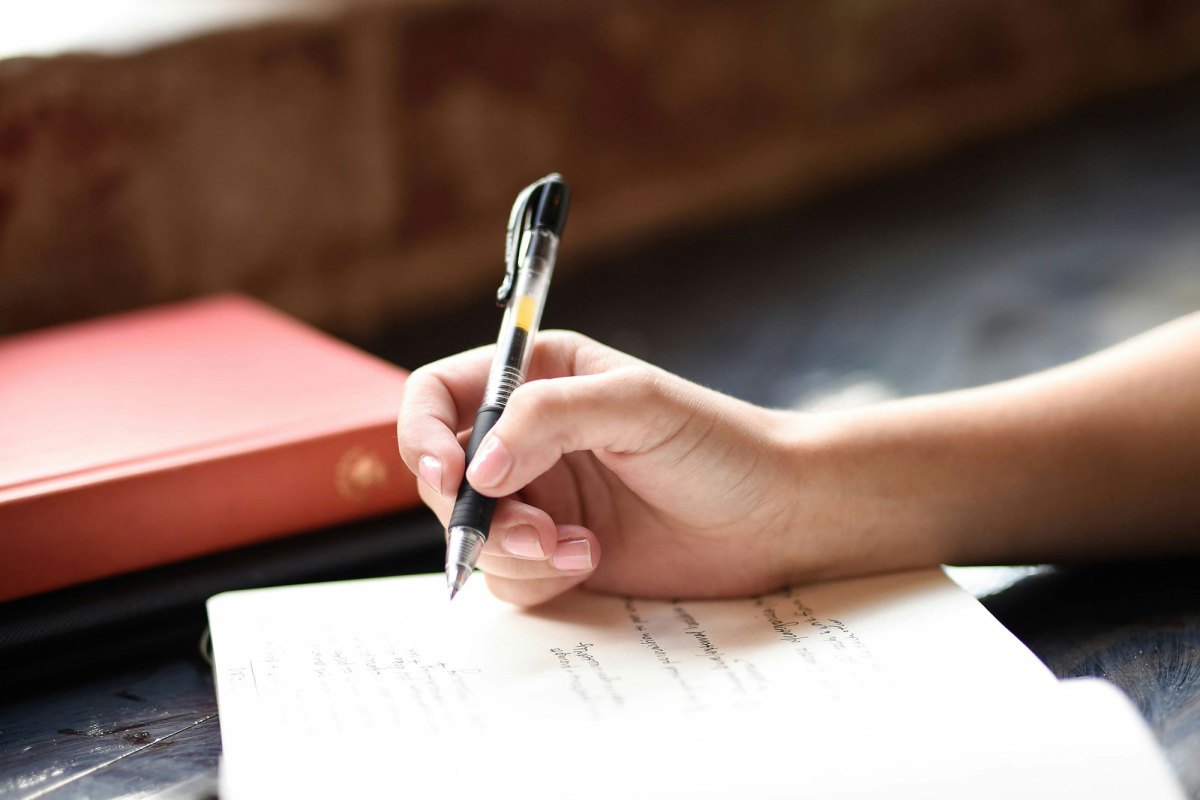 A hand holding a pen about to write on the page of a journal.