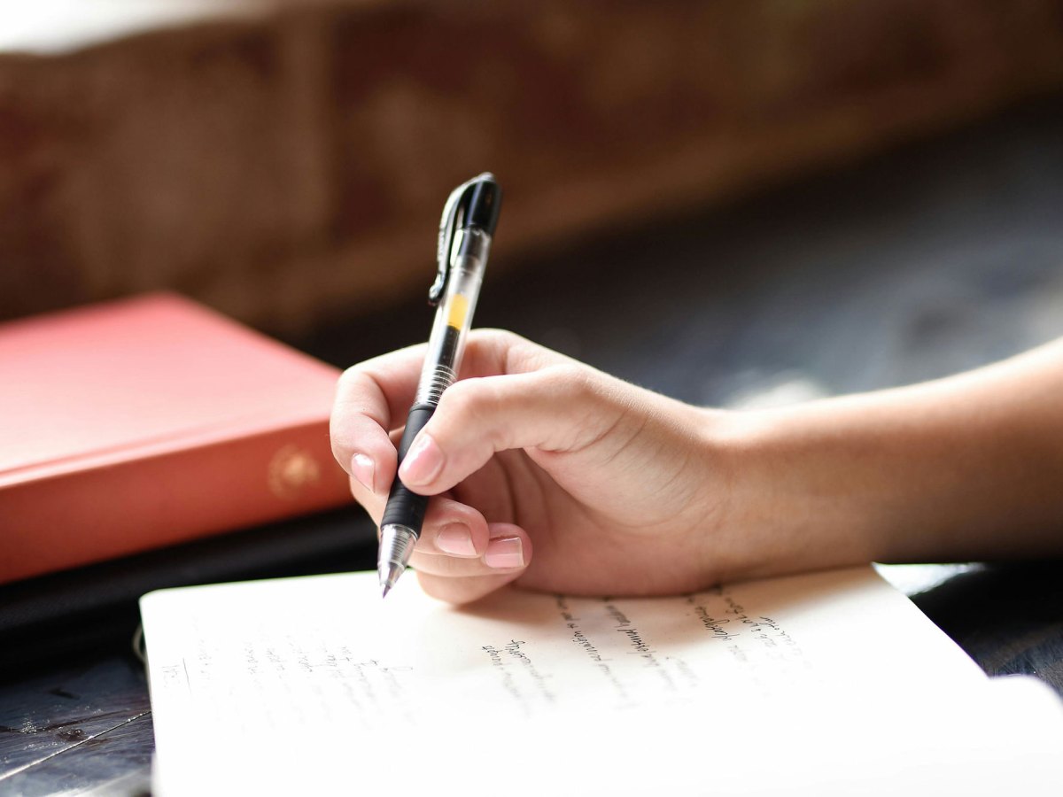 A hand holding a pen about to write on the page of a journal.