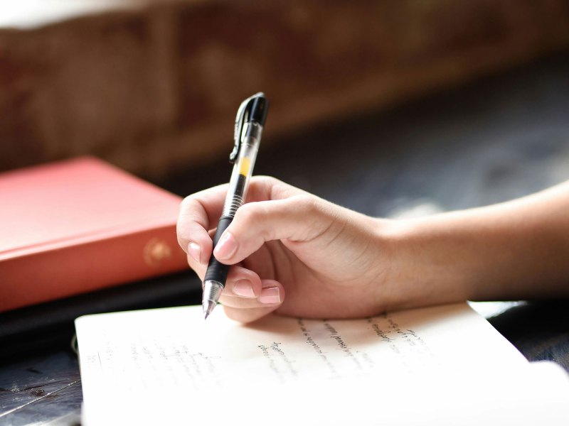 A hand holding a pen about to write on the page of a journal.