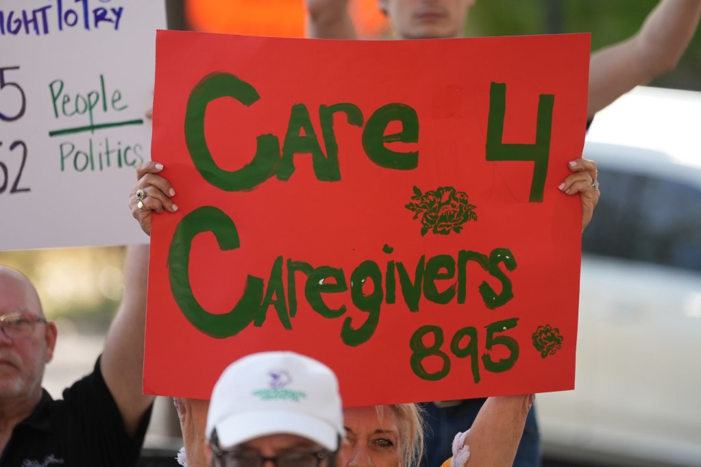 A person holds up a red sign that reads 'Care 4 Caregivers 895'