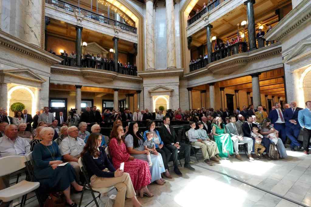 The Mississippi capitol building is filled with seated people in the first floor and standing people looking down from the second and third floor balconies
