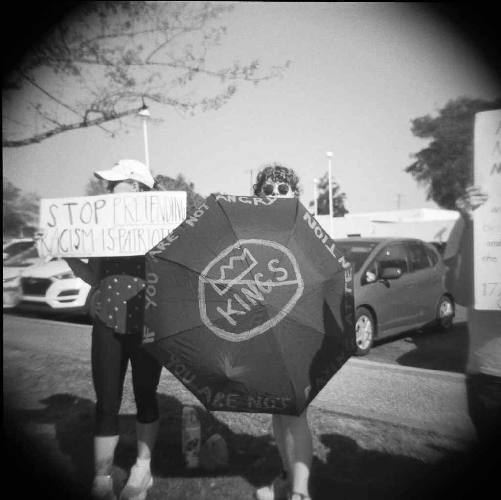 A protestor holds an umbrella up that reads NO KINGS