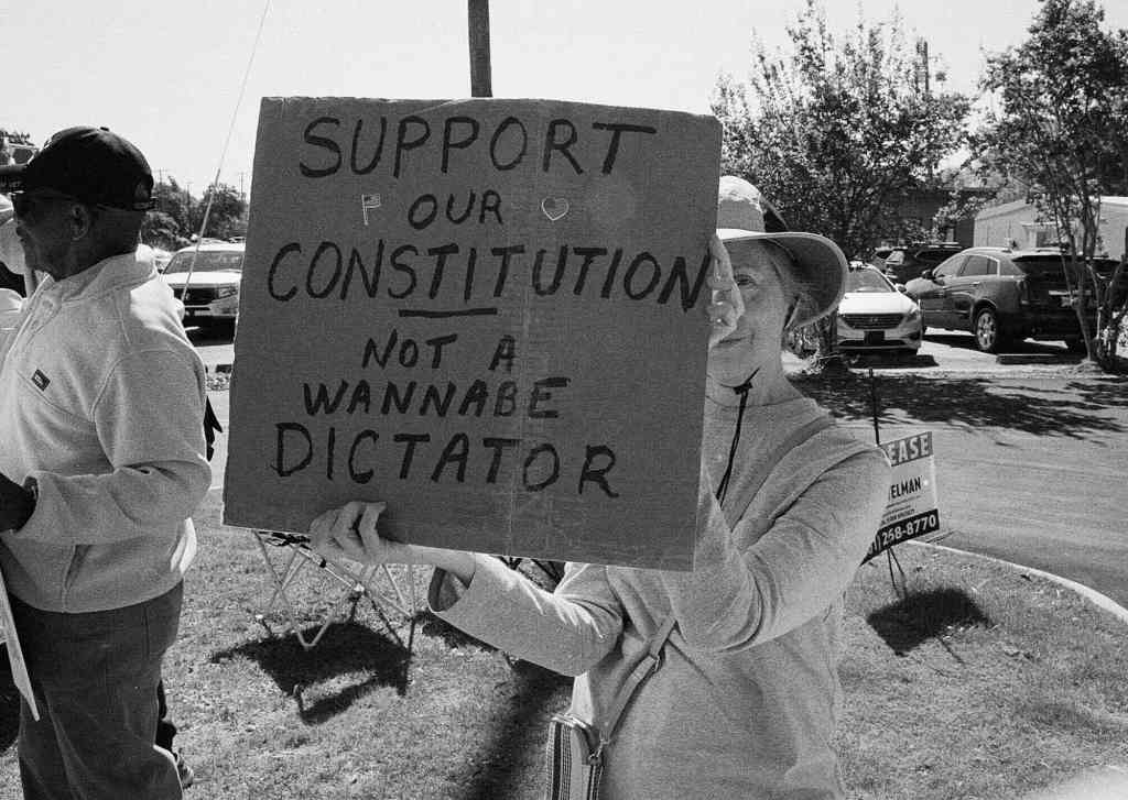A person holds a sign that reads 'Support our Constitution not a wannabe Dictator'