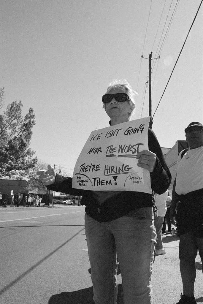 A person holds a sign by the road that reads 'ICE Isn't going for the WORST they're Hiring them!'
