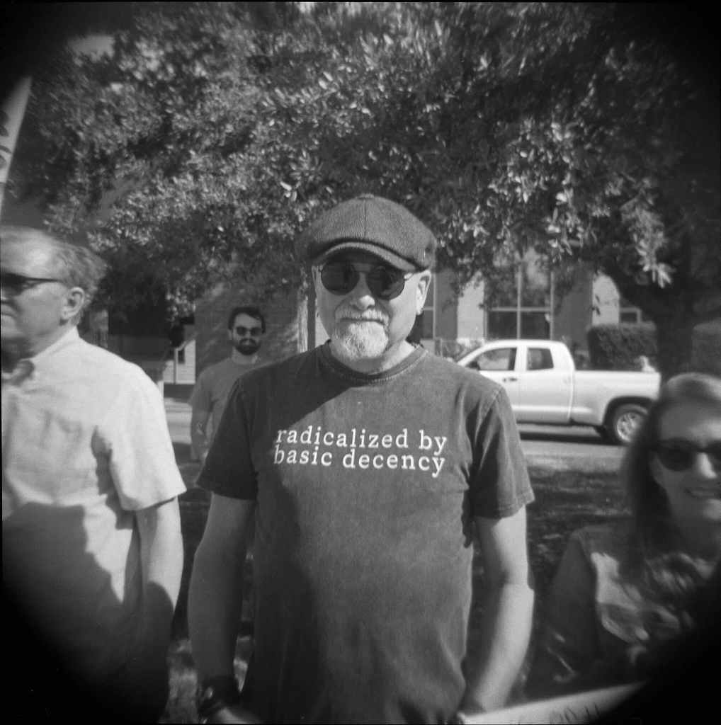 A man in cap and sunglasses wearing a tshirt that reads 'Radicalized by basic decency'