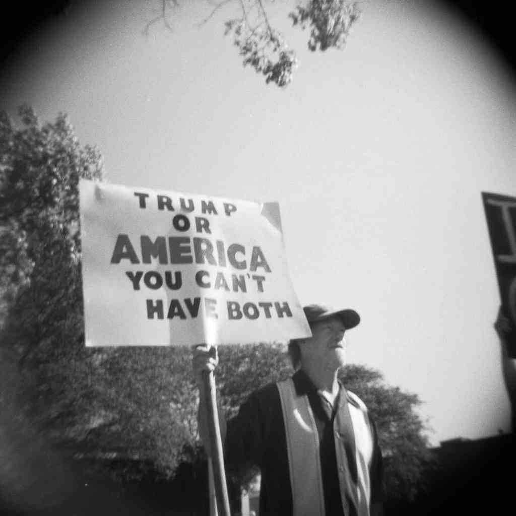 A person holds a sign that reads 'Trump or America You Can't Have Both'