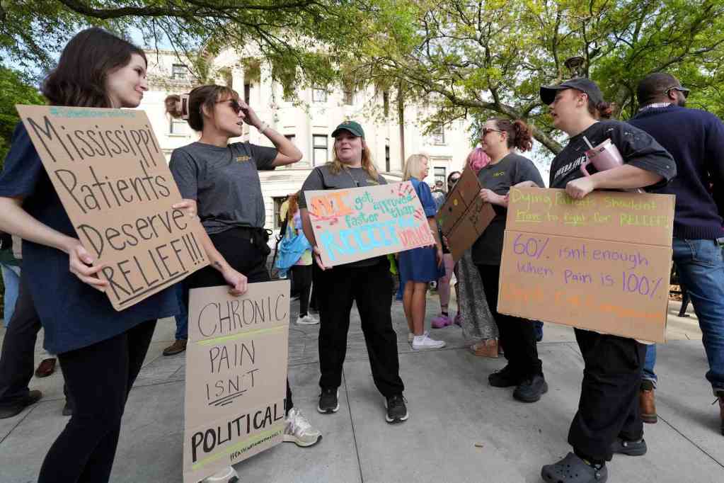 People gathered outside with signs written on brown cardboard that read 'Chronic Pain Isn't Political'