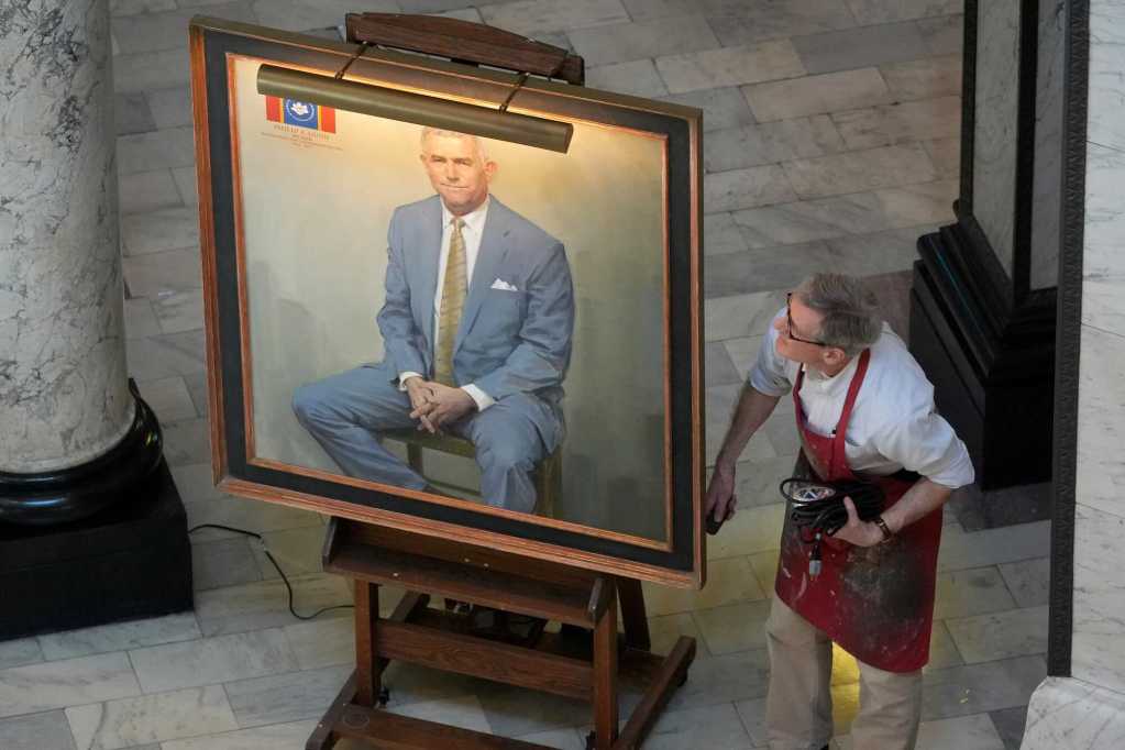 A portrait of Philip Gunn sits on a large easel as the artist looks on