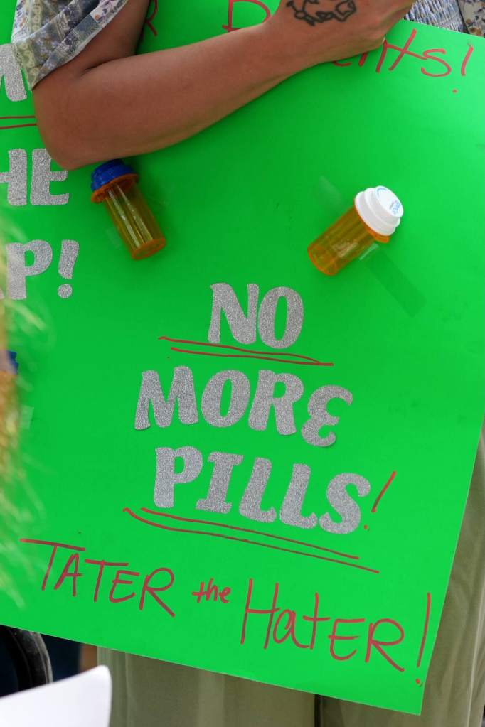 Closeup of a bright green sign that reads 'No More Pills! Tater the Hater!' with pill bottles taped to the sign