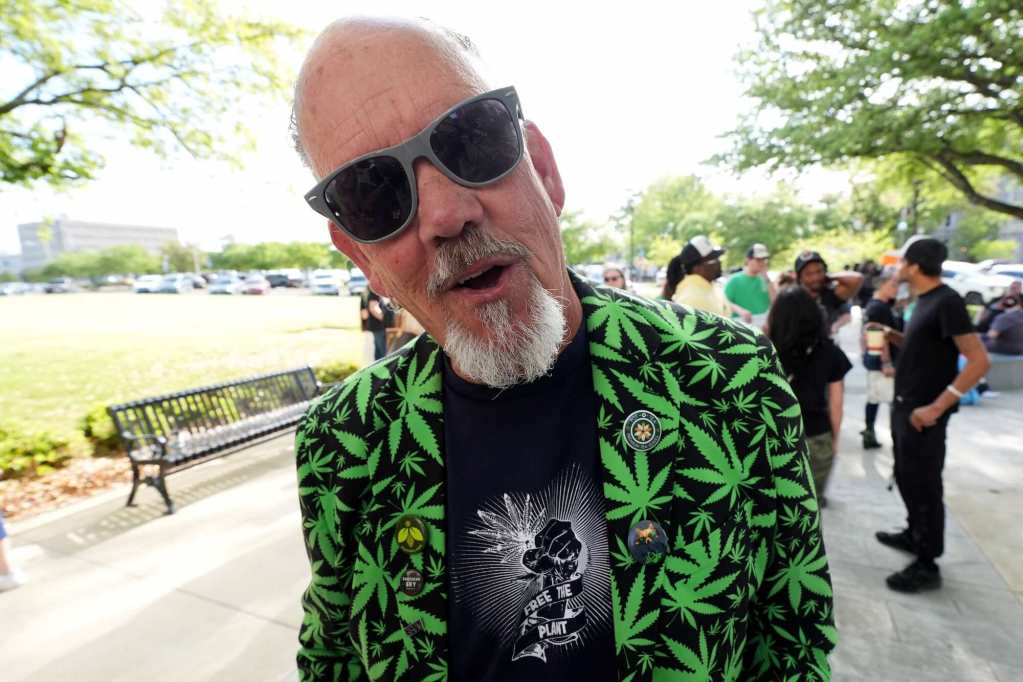 A man in a green and black suit covered in marijuana leaves looks into the camera