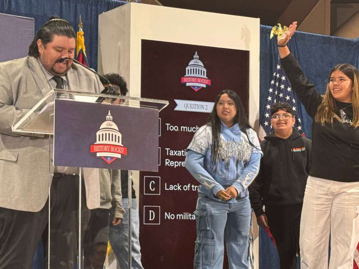People stand on stage for an event with signs that reads 'History Rocks!'