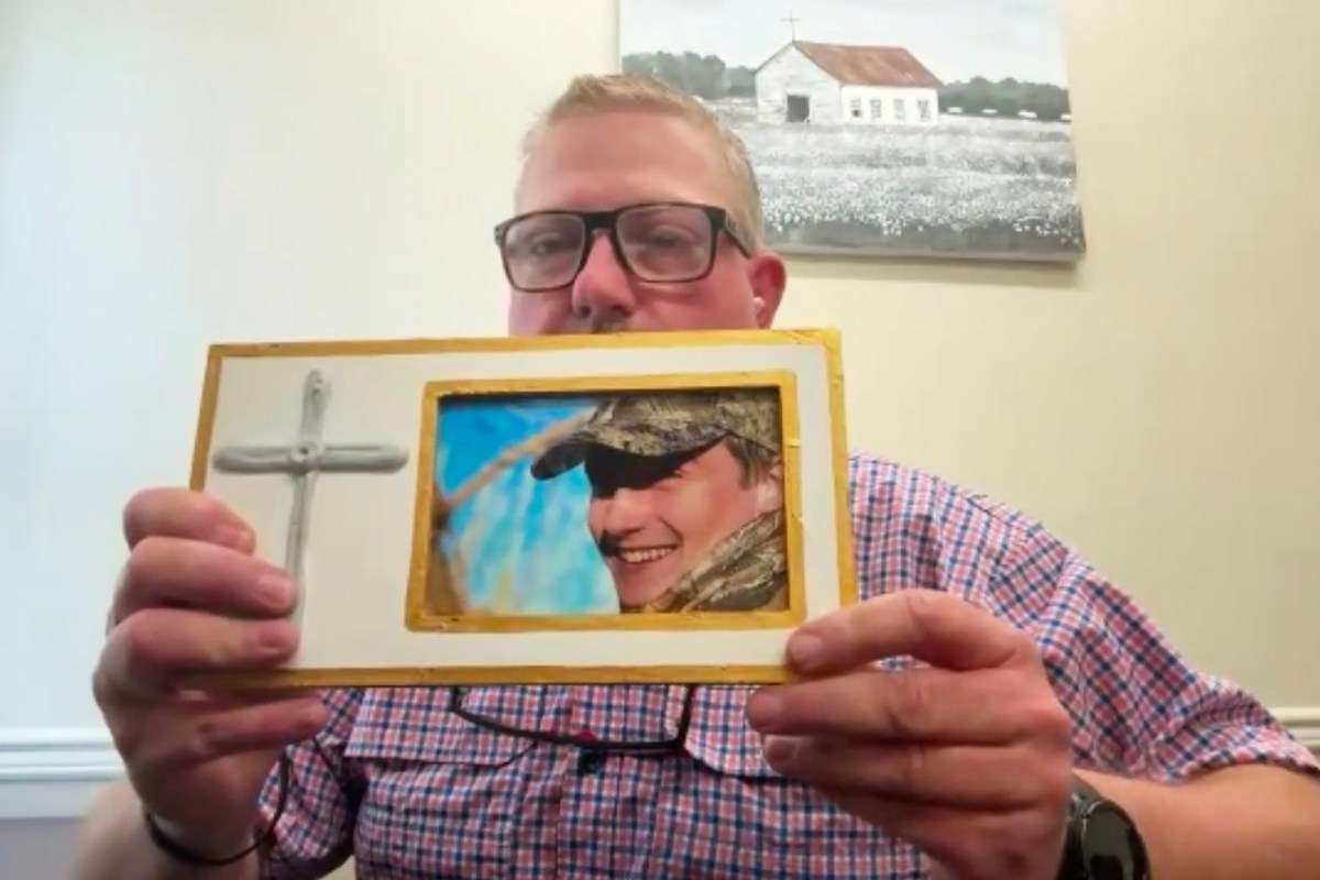 A man holds up a framed photo of his son