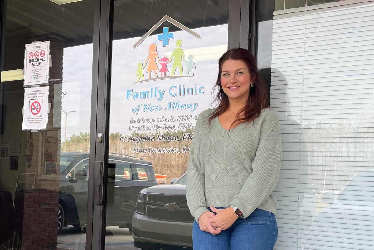 A woman with brown hair stands outside of a door labeled 'Family Clinic of New Albany'