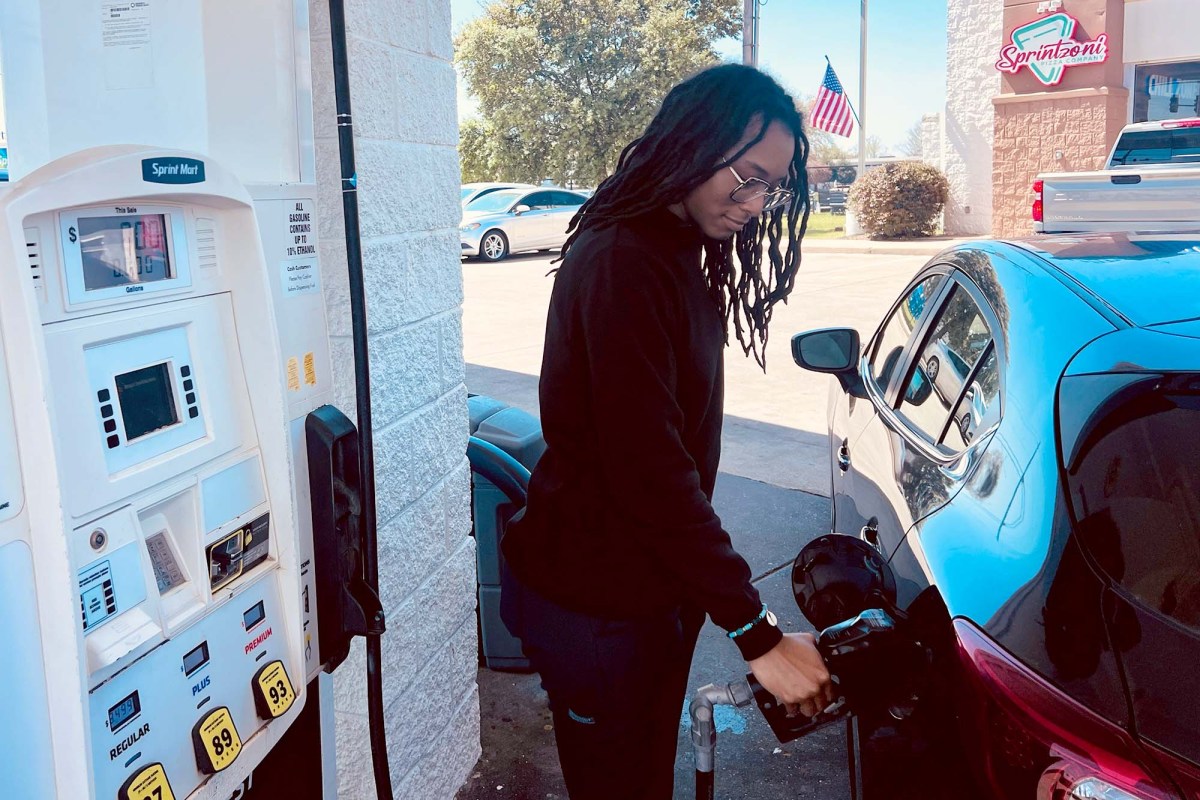 A black woman with locs pumps gas into a black car