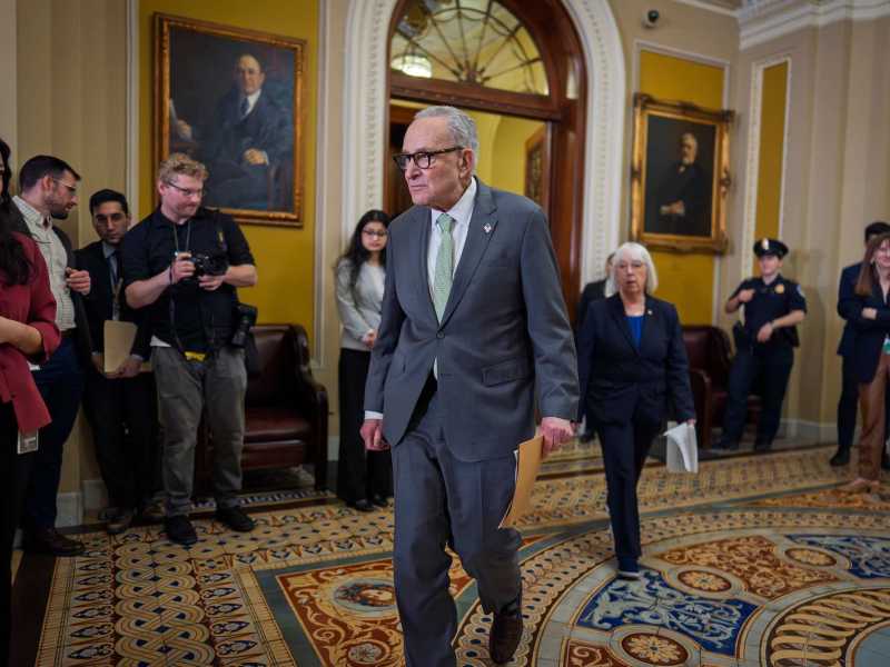Chuck Schumer walking in the U.S. Capitol building with several reporters in the background