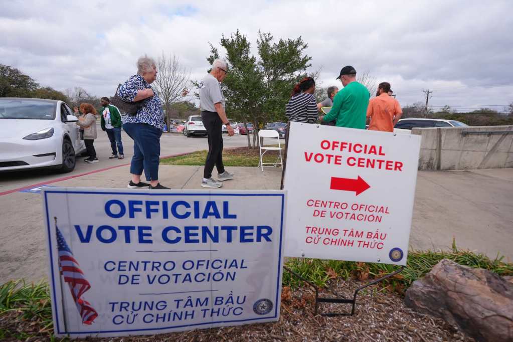 People arrive to a voting center, walking past two signs that label it as such