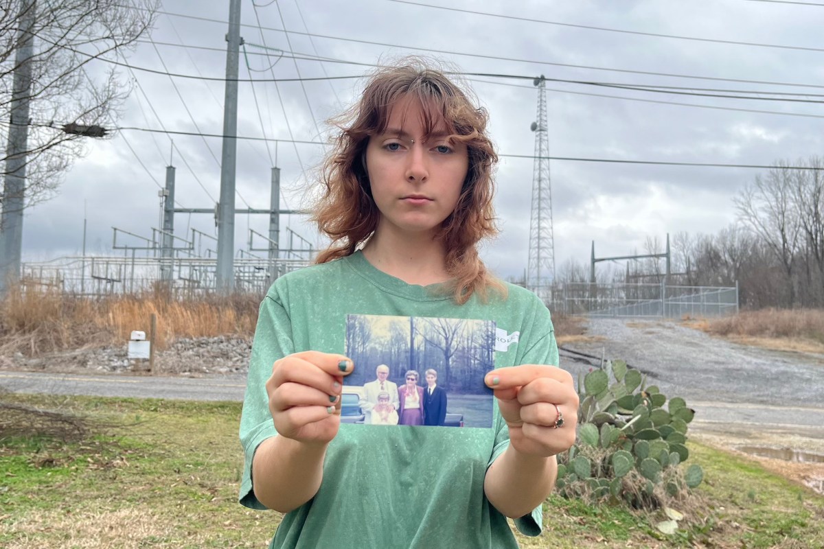 A person in a green shirt holds up a family photo in front of a fenced off zone