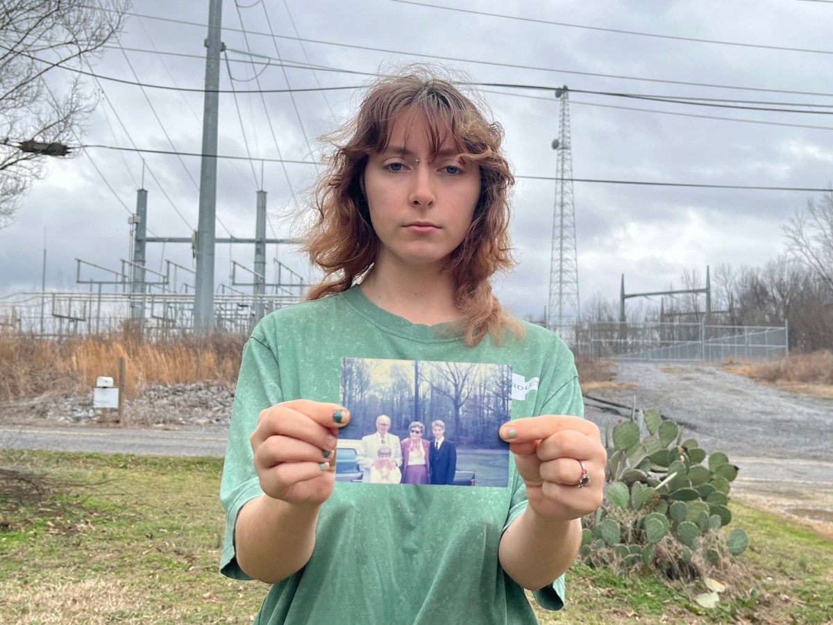A person in a green shirt holds up a family photo in front of a fenced off zone