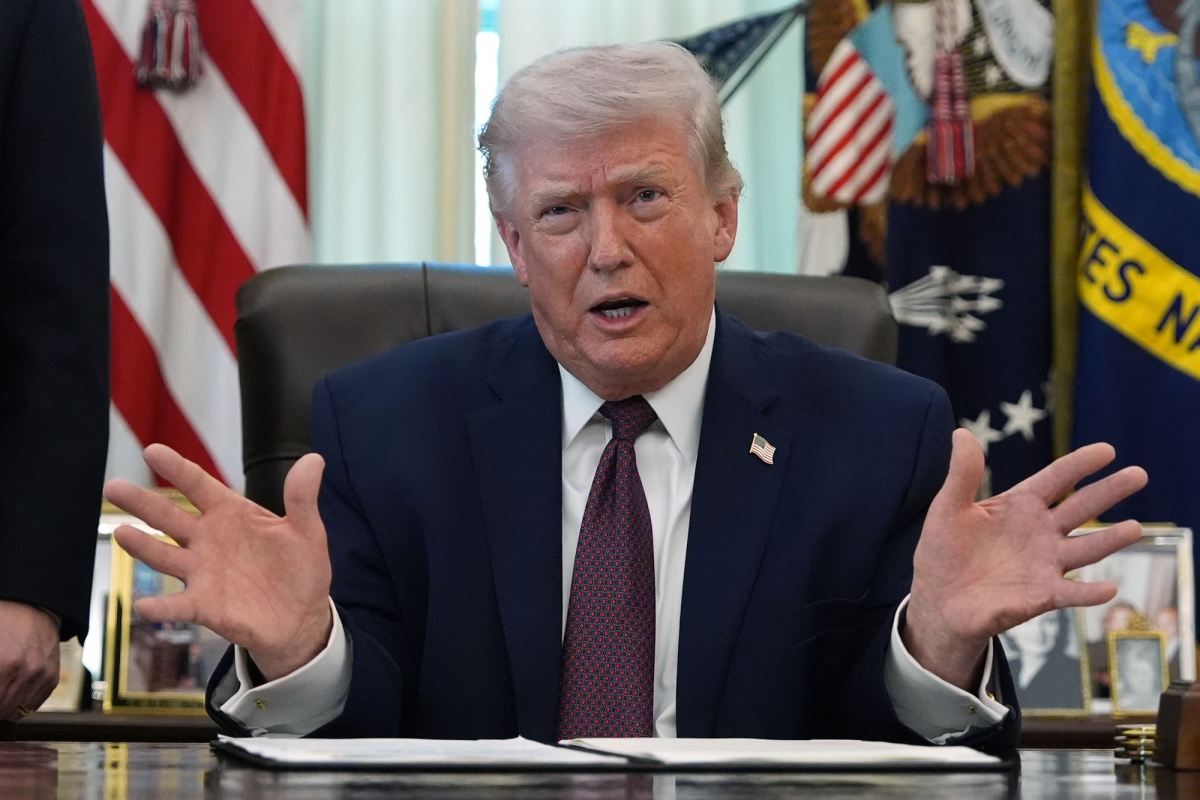 Donald Trump sitting at his desk, speaking with hands spread wide