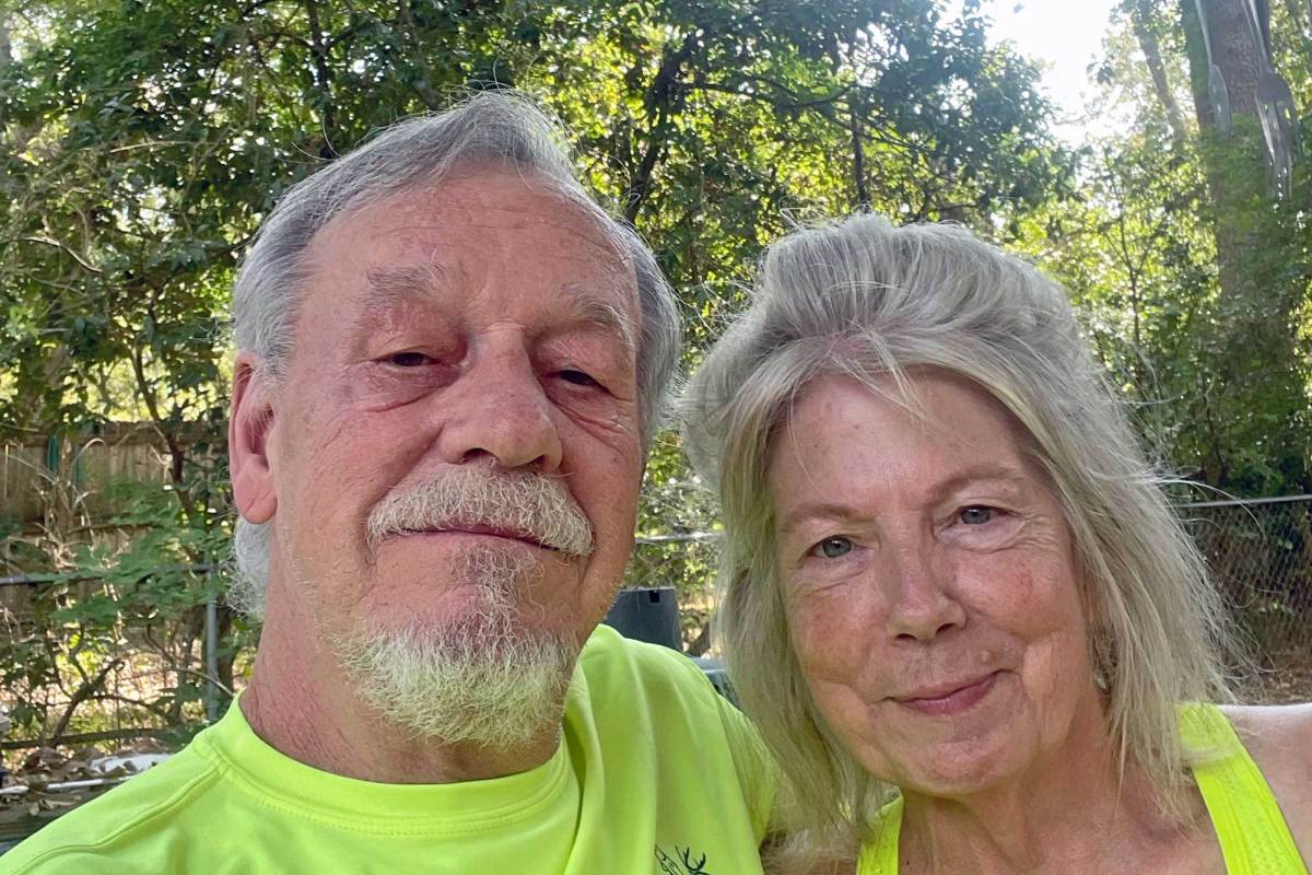 A man and woman in high-vis yellow tops posing for a phot Outside, trees visible behind them