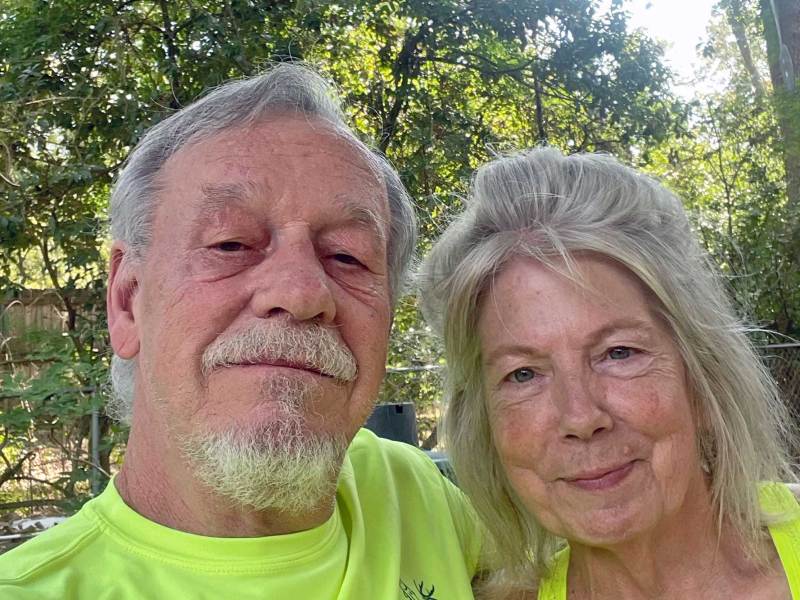 A man and woman in high-vis yellow tops posing for a phot Outside, trees visible behind them