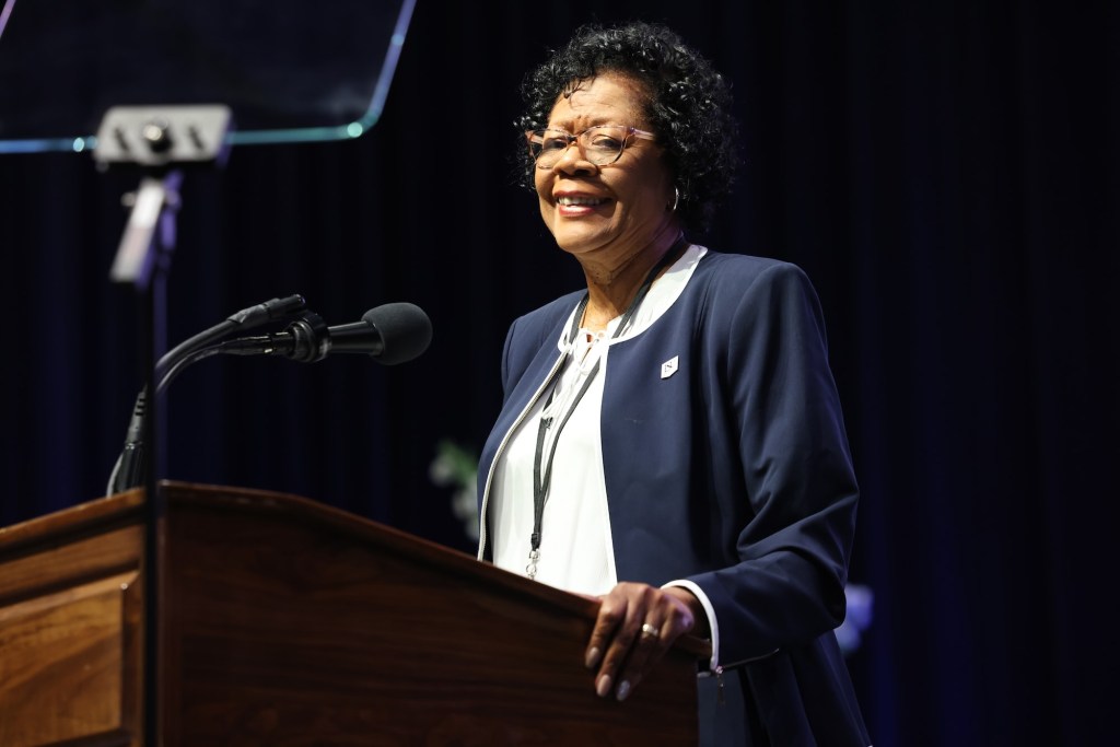 Elayne Hayes-Anthony and a navy blue and white suit speaking at a podium on a stage