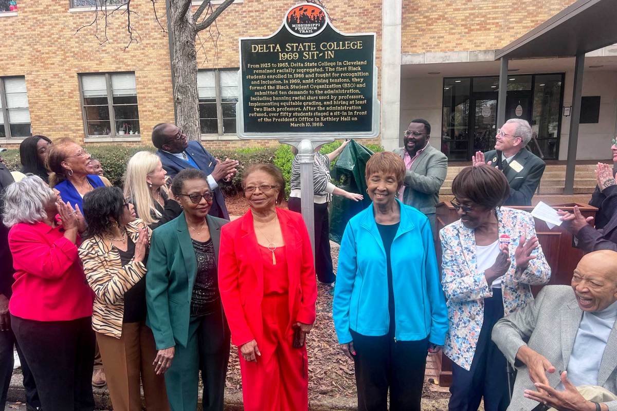 People clap and look on as a historical marker is uncovered. The marker is labeled 'Delta State College 1969 Sit-in'