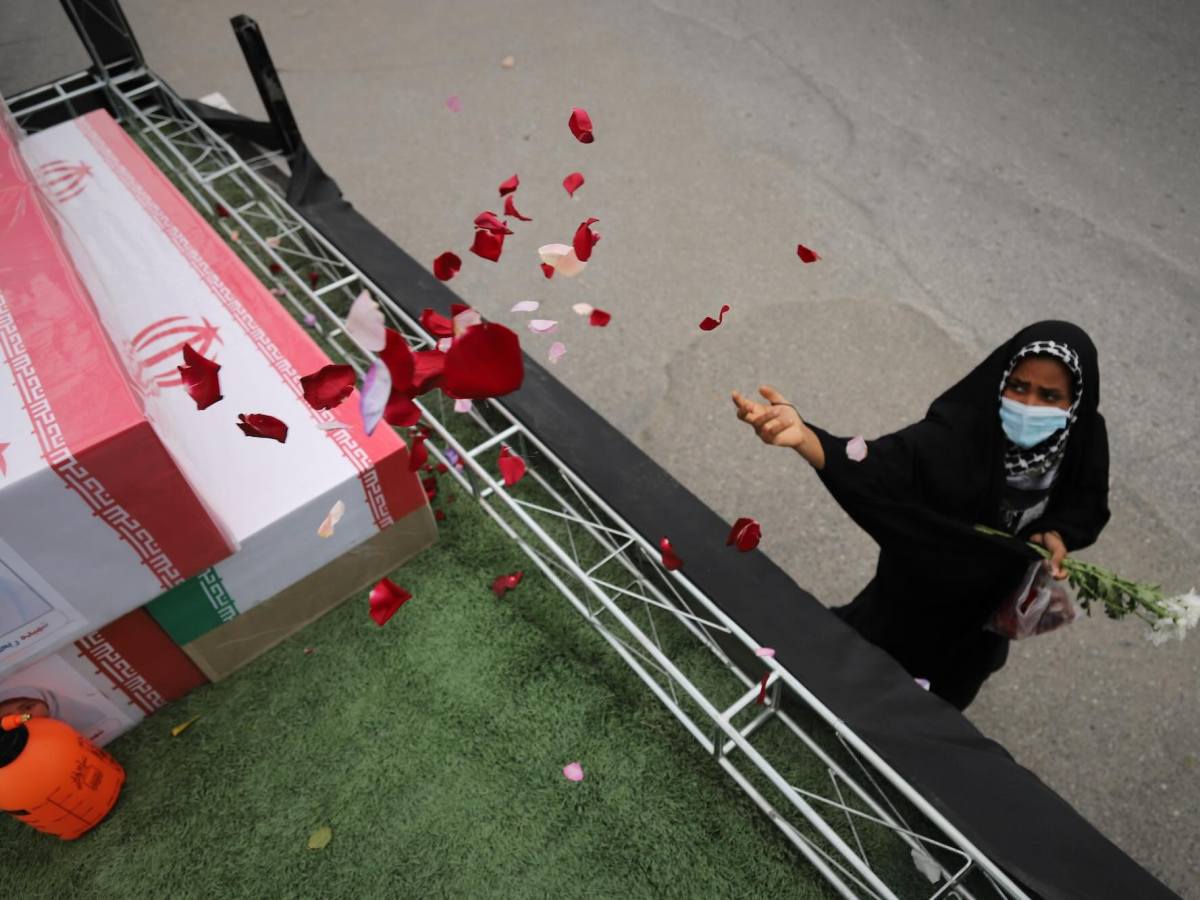 A woman throws flower petals onto coffins on a raised stage at a funeral
