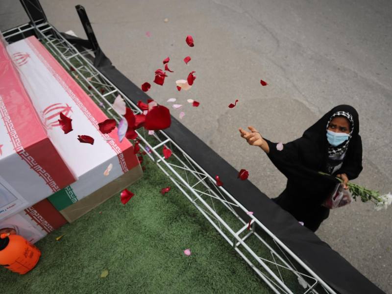A woman throws flower petals onto coffins on a raised stage at a funeral