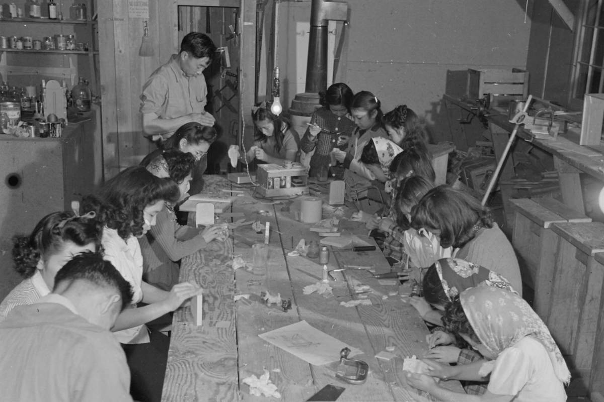 A black-and-white photo of several women seated at a table creating crafts.