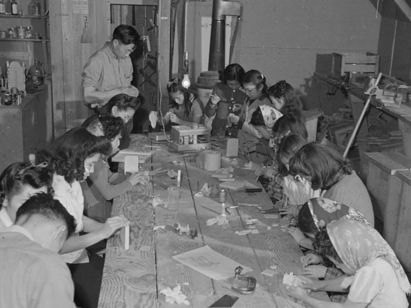 A black-and-white photo of several women seated at a table creating crafts.