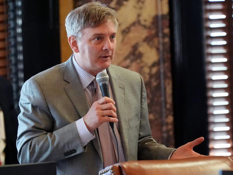 Joey Fillingane stands in the Mississippi Senate Chamber while holding a microphone in one hand.