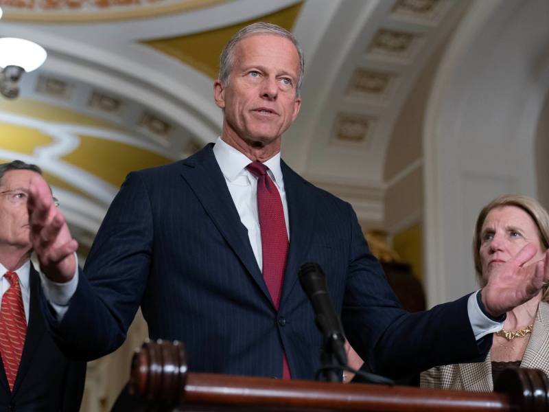 John Thune speaking at a podium with his arms out wide