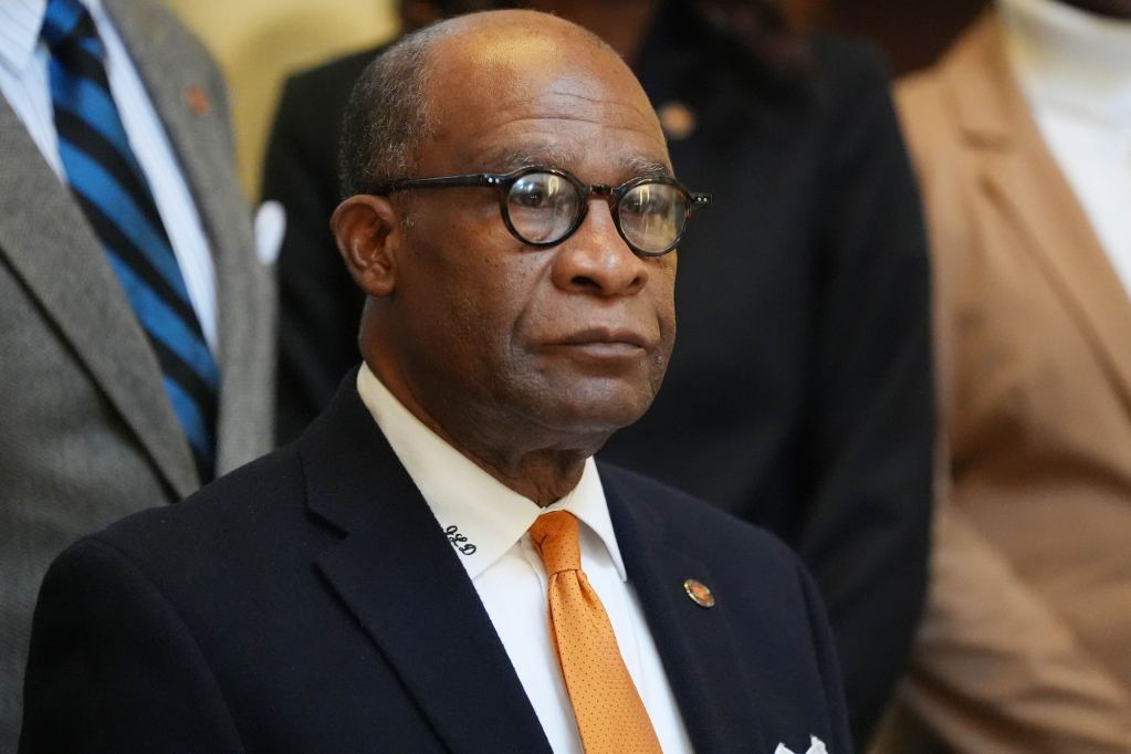 A closeup of Johnny Dupree in a crowd, wearing a dark suit with gold tie