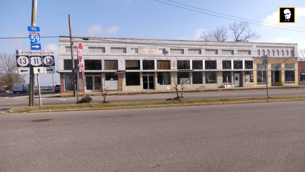 Row of older commercial buildings along a street in downtown Lumberton with traffic signs in the foreground.