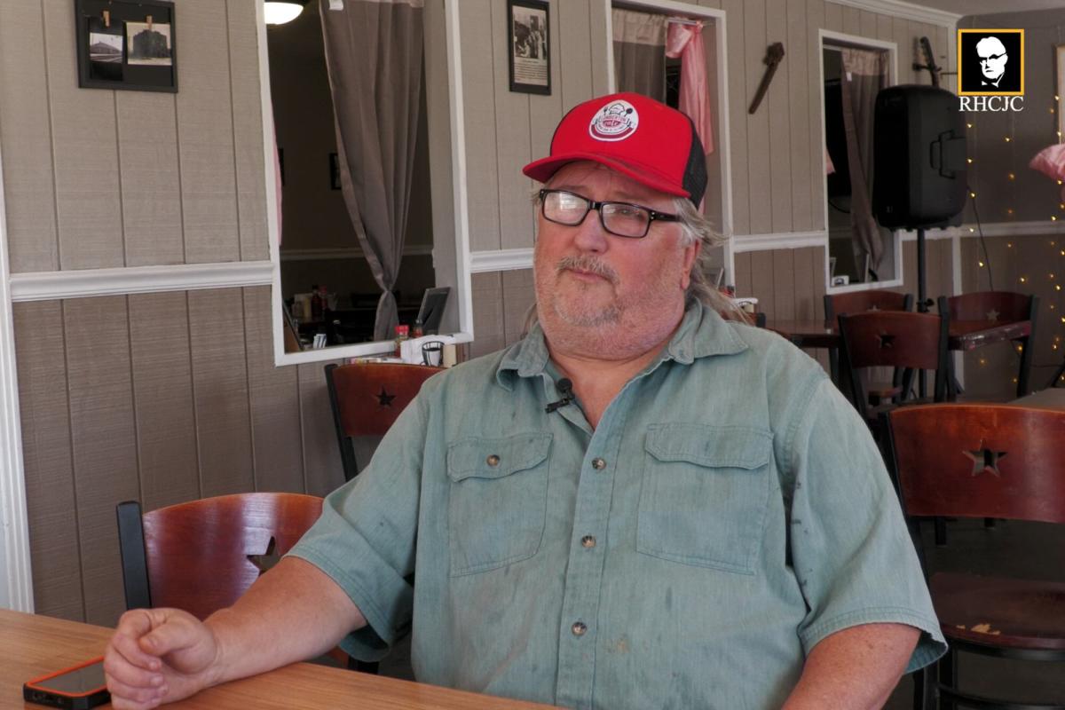 Alan Triplett sits at a table inside Lumberton Cafe wearing a red cap and glasses during an interview